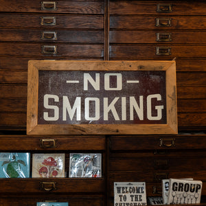A brown "No Smoking" sign rests against a chest of drawers.