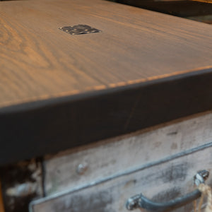 A side view of the wooden top on a refurbished metal hospital cart, with a focus on a metal inlay. 